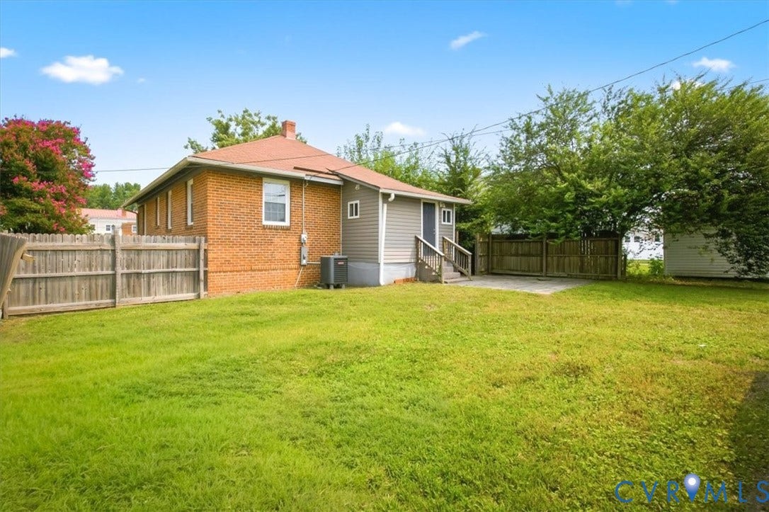 125 Richmond Avenue, Colonial Heights, VA 23834 Expansive grassy backyard featuring a partial wood fence, a concrete patio area, and mature perimeter trees