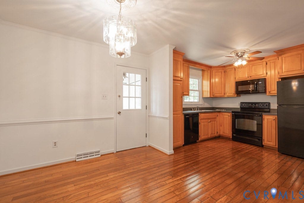 Open-concept kitchen and dining area featuring wood-finish flooring, light wood cabinetry, black appliances, a ceiling fan, and a glass-paneled door