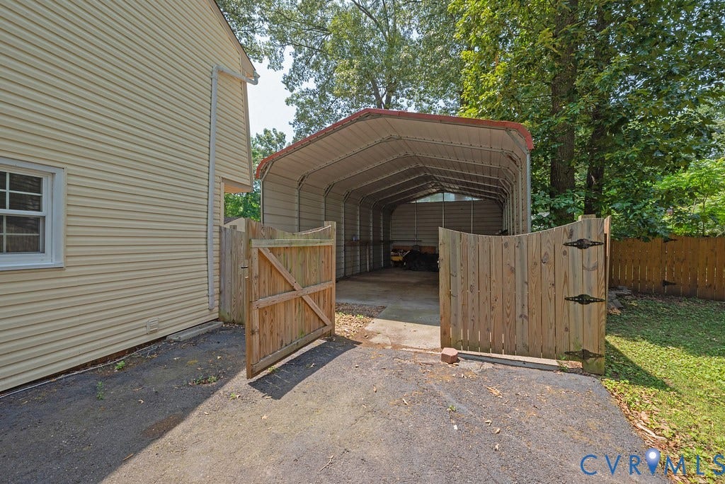 Carport with metal roof and concrete floor, bordered by a wooden privacy fence and a siding exterior