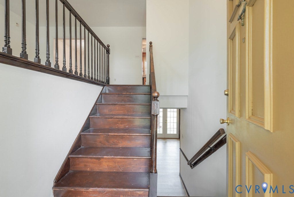Entryway featuring a wood staircase with baluster railing, an open doorway, and a lower-level corridor with French doors