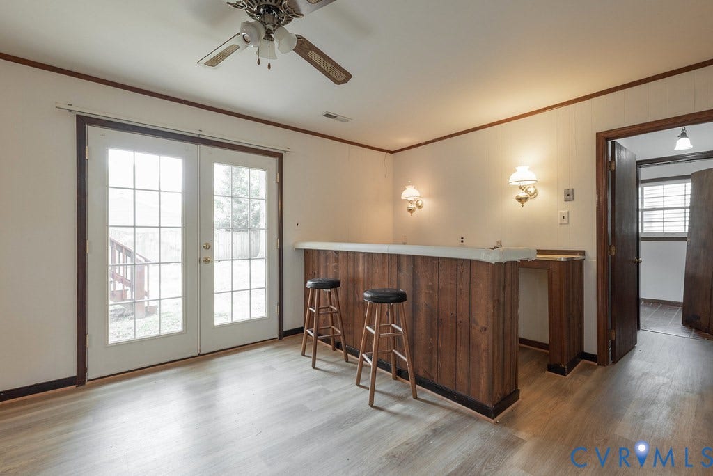 Interior space featuring light wood-finish flooring, a built-in wood-paneled bar with sconce lighting, and French doors leading to exterior stairs