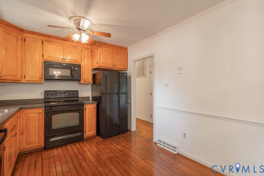 Kitchen featuring wood-finish flooring, light wood cabinetry, black appliances, and a ceiling fan with integrated lighting