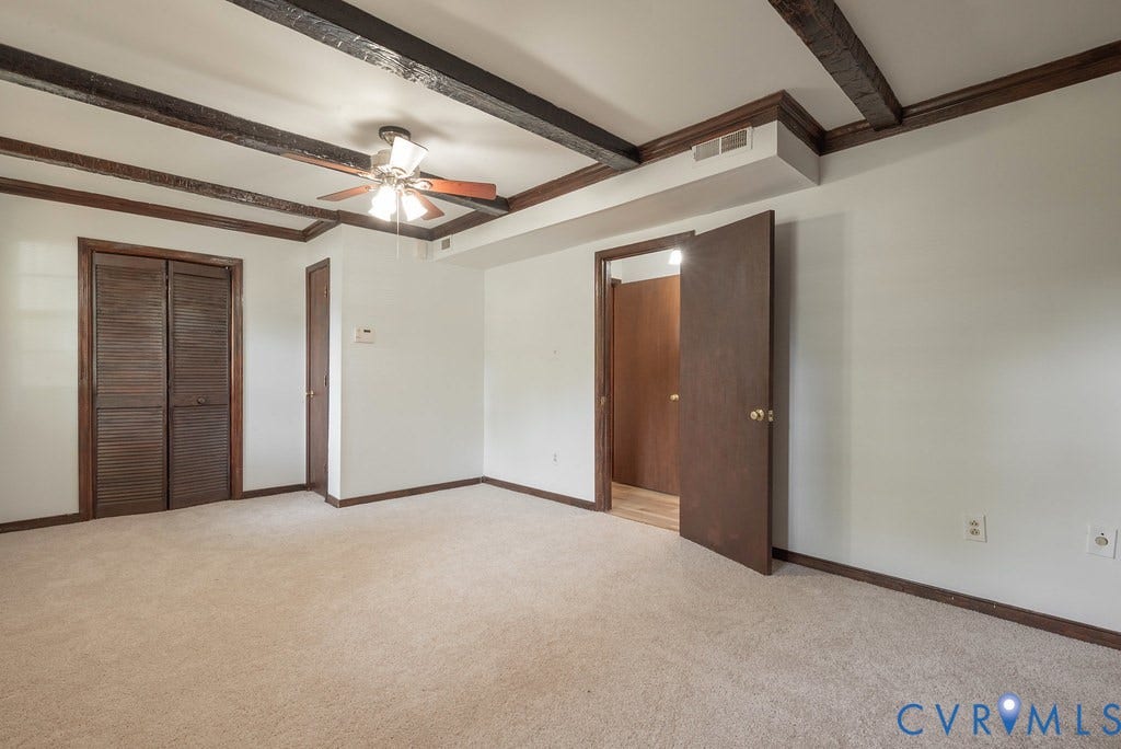 Interior room featuring exposed wood ceiling beams, a ceiling fan with light fixture, carpeted flooring, and white painted walls