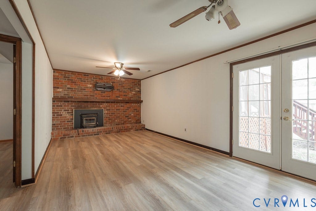 Spacious room featuring wood-finish flooring, a brick accent wall with a built-in fireplace, and double French doors providing exterior access