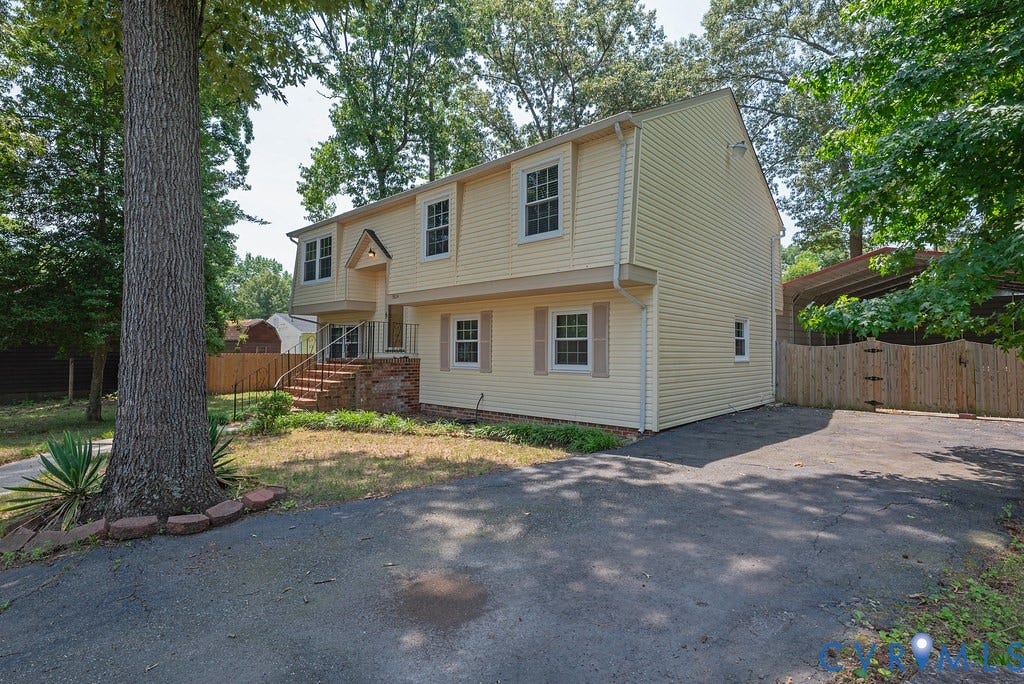 Split-level residence featuring light-colored siding and white-framed windows with decorative shutters