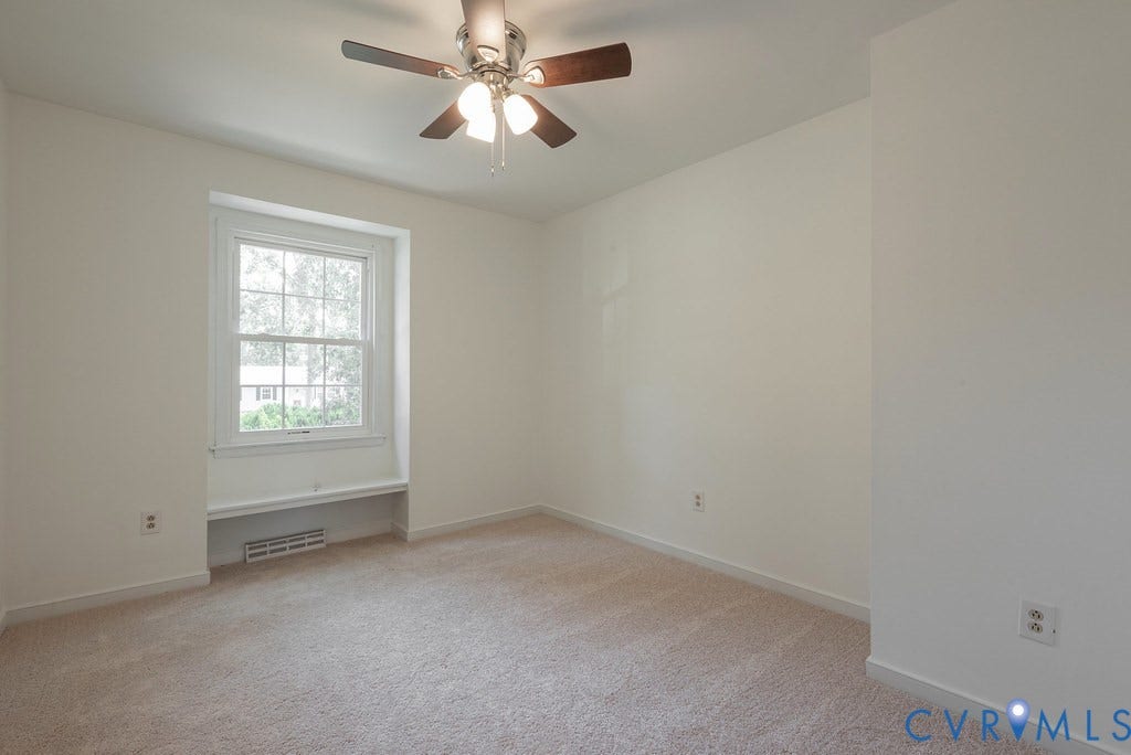 Room featuring neutral carpet flooring, white walls, a multi-pane window, a recessed window bench, and a ceiling fan with integrated lighting