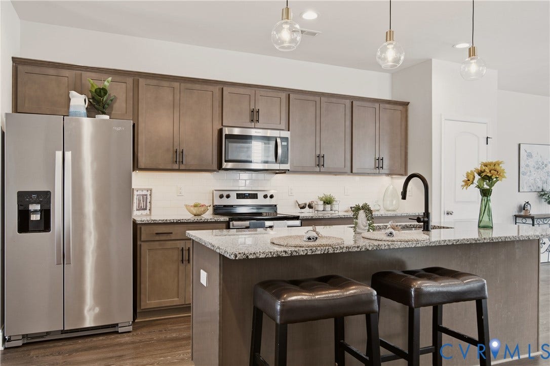 Kitchen featuring stainless steel appliances, granite countertops, subway tile backsplash, wood-finish flooring, and pendant lighting