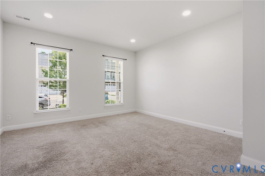 Spacious room featuring two large windows, recessed ceiling lighting, light gray wall paint, and gray carpet flooring
