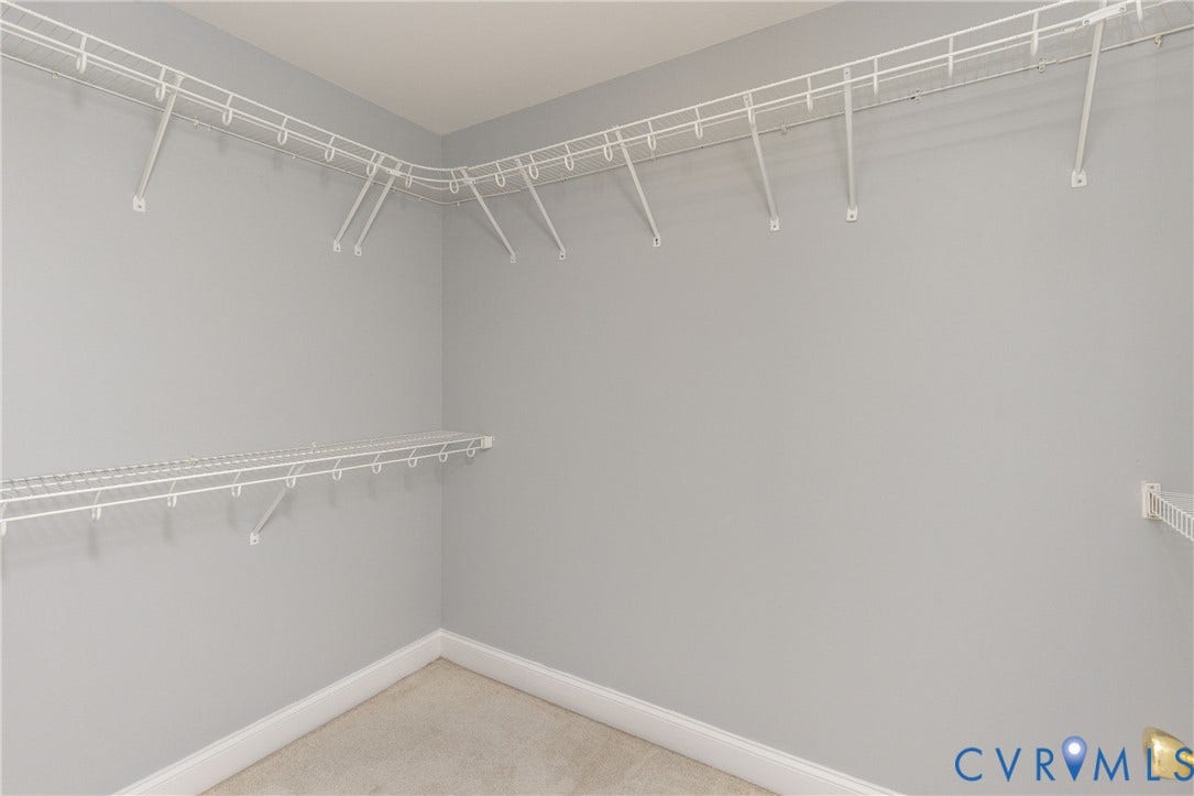 Closet space featuring light gray wall paint, white wire shelving, white wire hanging rods, and light-colored carpet flooring