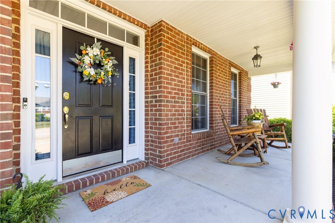 Brick facade residence featuring a covered front porch with a concrete surface, white column support, and a black paneled front door with sidelights and transom windows