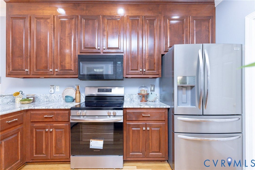 Kitchen featuring wood-finish cabinetry, light-toned countertops, and stainless steel appliances including a refrigerator, range, and microwave