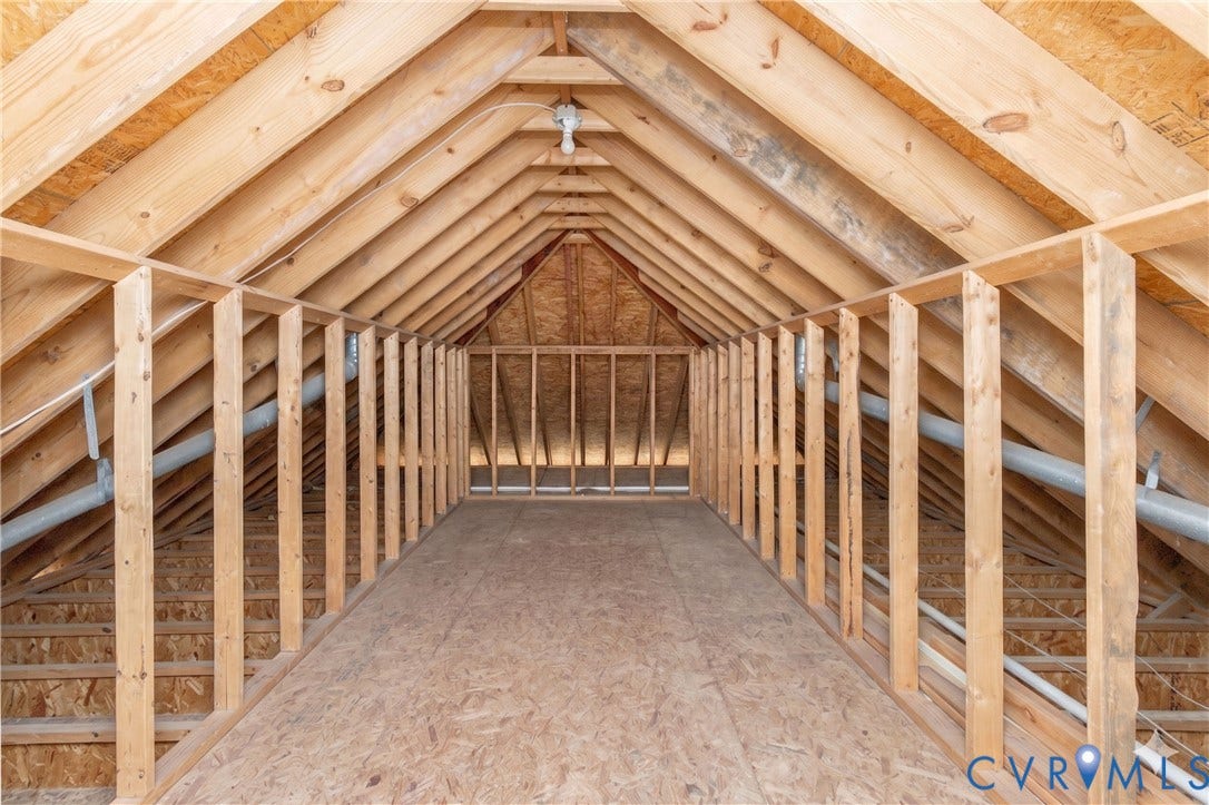 Spacious unfinished attic space featuring exposed wood framing, wood-finish flooring, and a peaked ceiling