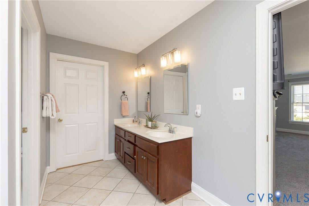 Bathroom featuring a dual vanity with a white countertop and wood-finish cabinetry, illuminated by a three-bulb fixture