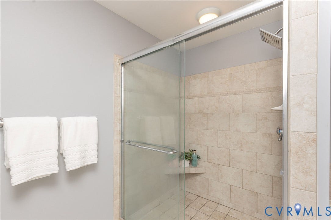 Shower enclosure featuring a square rain shower head, light-toned wall tiling, built-in shelving, glass sliding doors, and complementary floor tiling