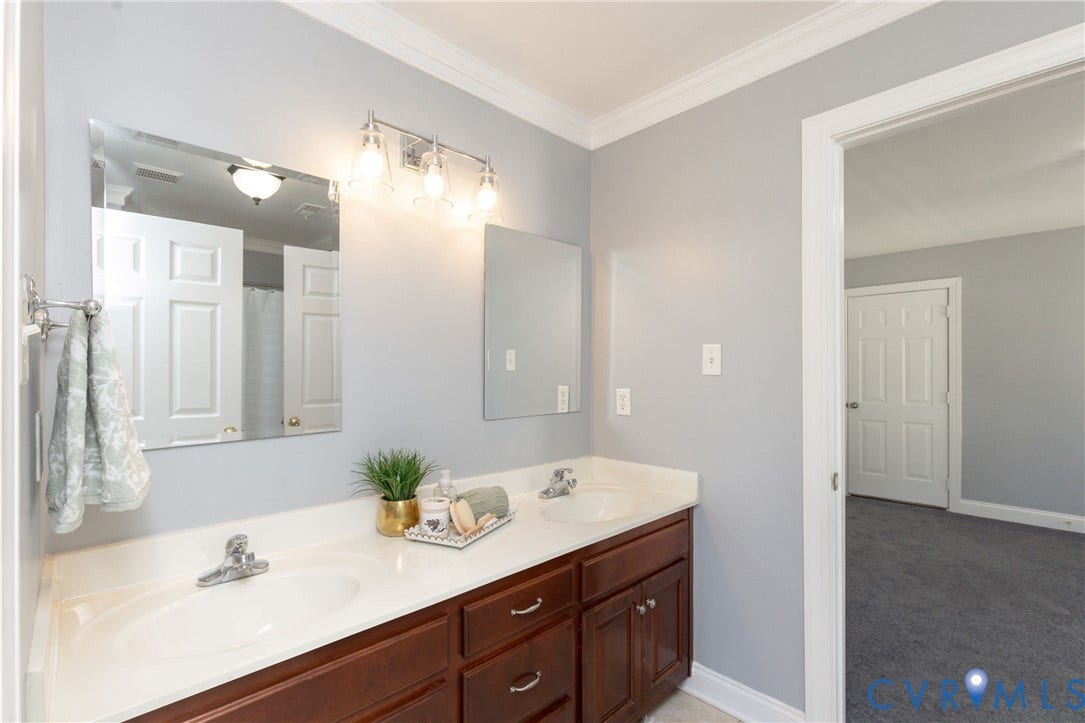 Bathroom vanity with dual sinks, chrome fixtures, integrated lighting, and a large wall-mounted mirror