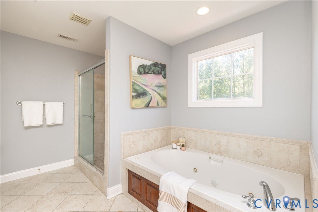Bathroom featuring a built-in jetted tub with tile surround, a glass-enclosed shower, and tile flooring