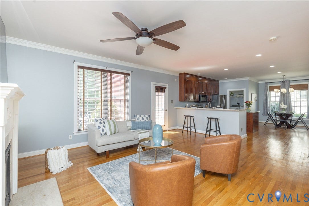 Expansive living area featuring hardwood flooring, a white mantel, and crown molding