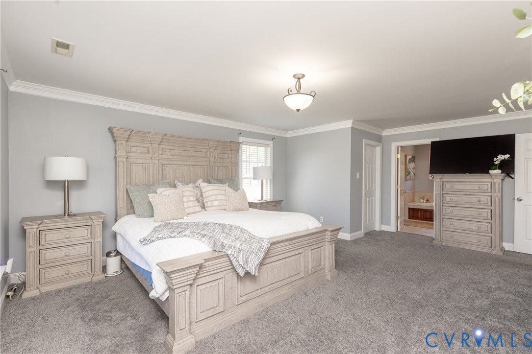 Spacious bedroom featuring light gray walls, white crown molding, and gray carpeted flooring