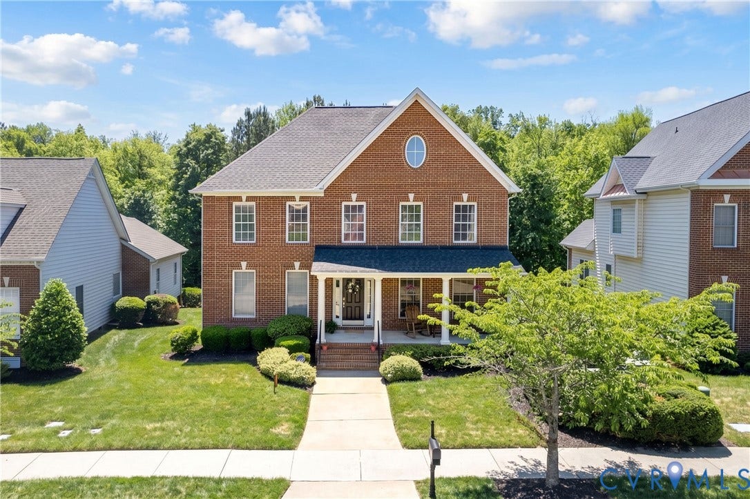 Traditional brick facade residence featuring a covered front porch, a second-story oval window, multiple pane windows, established landscaping, and a concrete pathway