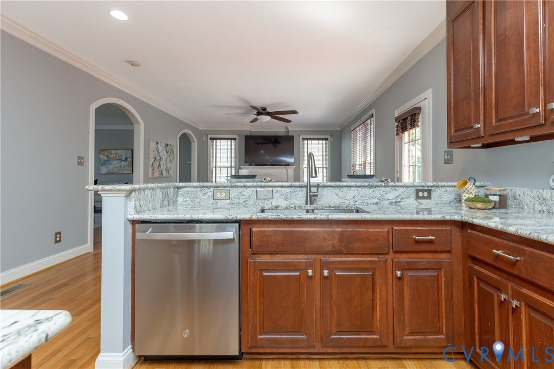 Kitchen featuring wood cabinetry, stainless steel dishwasher, an undermount sink with a gooseneck faucet, and light-toned granite countertops