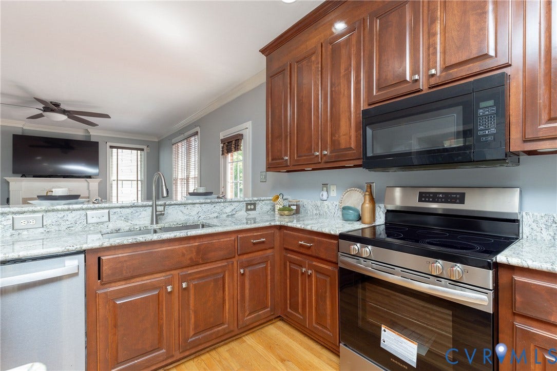 Kitchen featuring wood-finish flooring, stone countertops with a matching backsplash, stainless steel appliances, and wood cabinetry