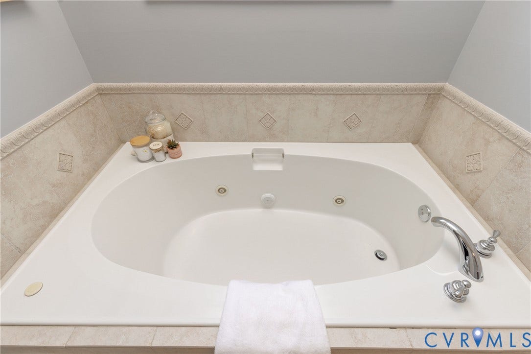 Built-in soaking tub with integrated jets, surrounded by neutral-toned tiled walls with decorative accents and a matching tiled deck