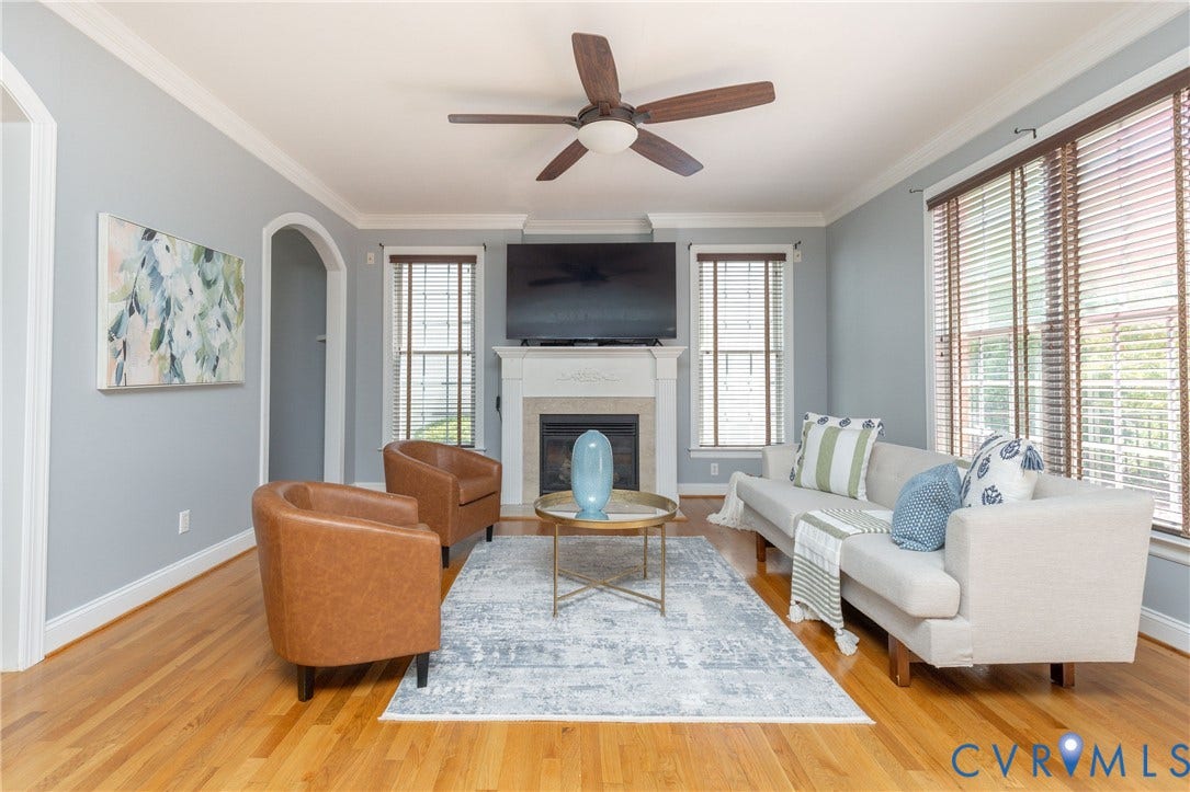Living area featuring hardwood flooring, a fireplace with a mantel, multiple windows with blinds, an arched doorway, and a ceiling fan