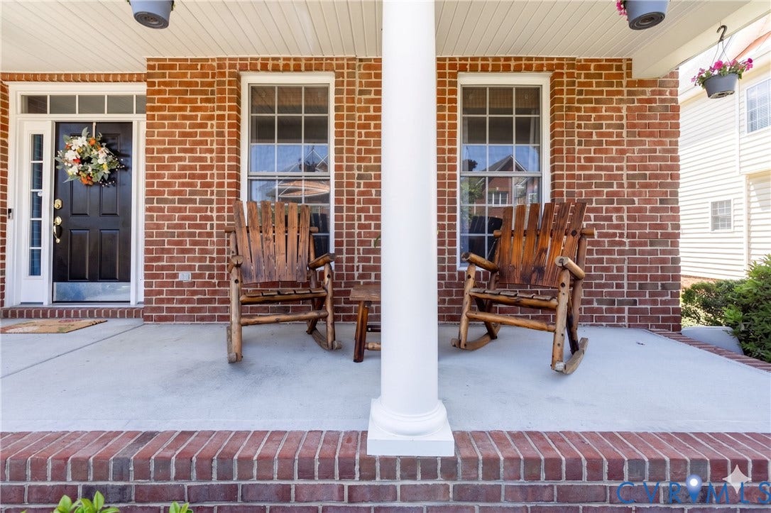 Brick facade entryway featuring a black front door with sidelights, transom window, and a concrete porch with a white structural column