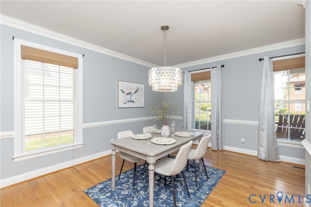 Dining area featuring hardwood flooring, light blue wall color with white chair rail molding, and multiple windows with woven Roman shades