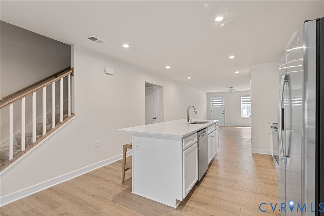 7213 Lyon Taylor Lane, Summer Maple, New Kent, VA 23124 Open-concept kitchen featuring a spacious island with a sink, white cabinetry, stainless steel appliances, and wood-finish flooring throughout