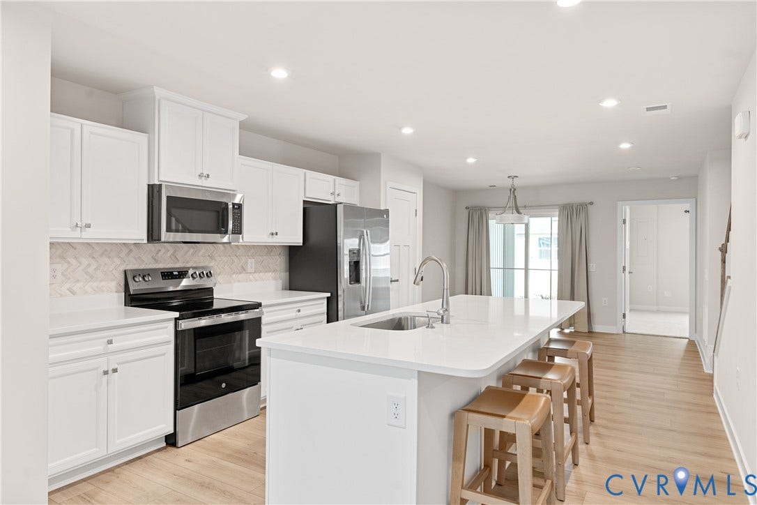7213 Lyon Taylor Lane, Summer Maple, New Kent, VA 23124 Modern kitchen featuring white cabinetry, a herringbone tile backsplash, stainless steel appliances, a large island with an undermount sink, and wood-finish flooring