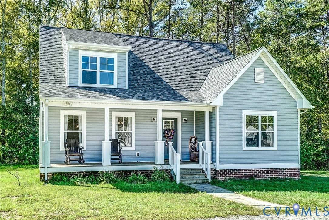 65 Hopeful Church Lane, Bumpass, VA 23024 Gray siding residence featuring a covered front porch with white columns, a dormer window, a shingled roof, a brick foundation, and a concrete pathway leading to the entrance