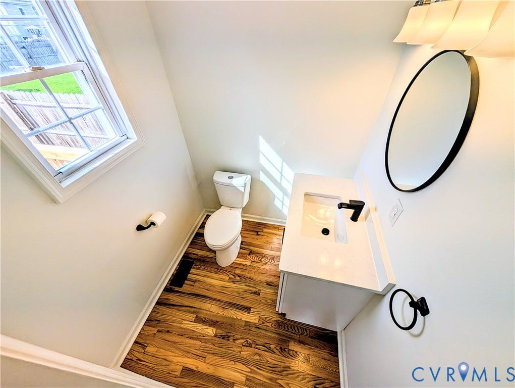 3216 Enslow Avenue, Richmond, VA 23222 Powder room featuring wood-finish flooring, a contemporary white vanity with integrated sink, a sleek black faucet, and a modern circular mirror