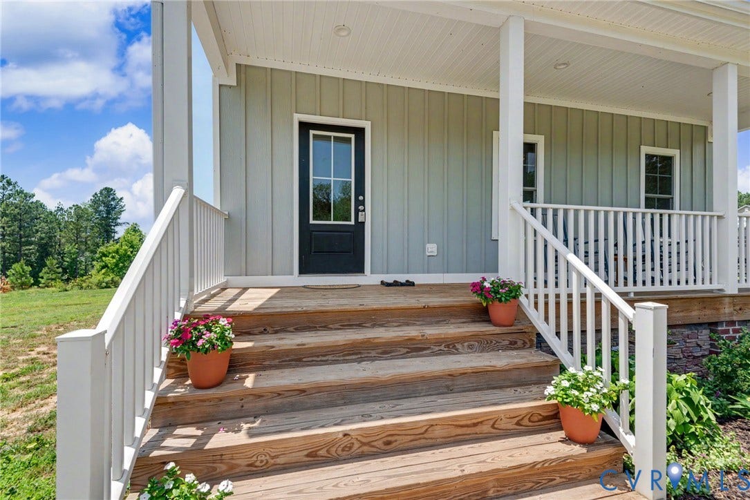 815 Kennon Road, Northeast Creek Reservoir Subd, Mineral, VA 23117 Wood-finish porch steps leading to a covered porch with white railing, light-colored board and batten siding, and a black entry door with transom window