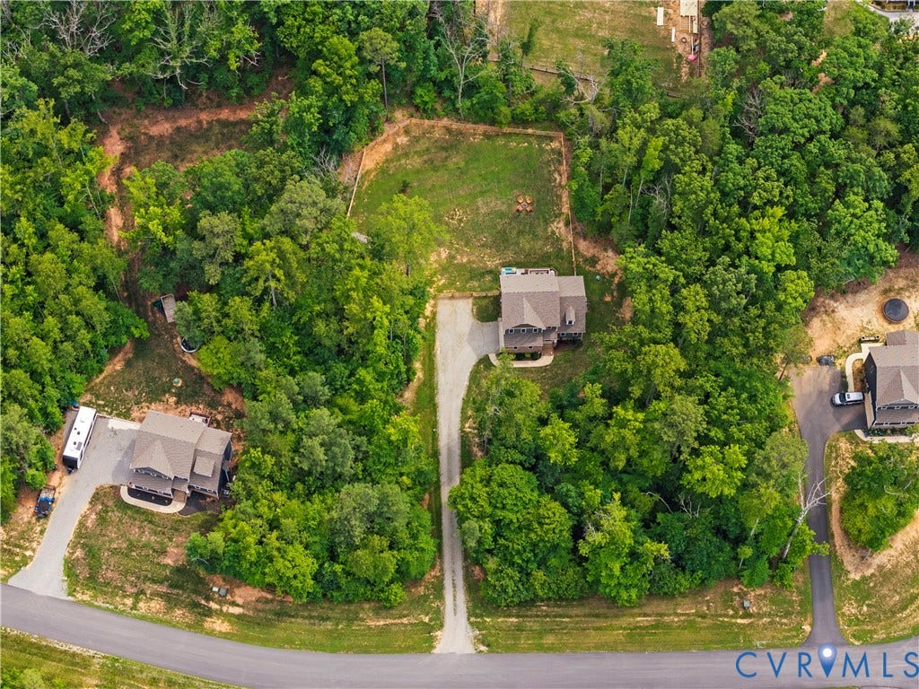 Expansive wooded lot featuring a multi-level residence with a gray shingle roof, a long gravel driveway, and a cleared yard space