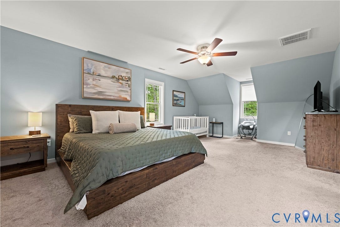 Spacious bedroom featuring light blue walls, soft carpet flooring, and a ceiling fan with integrated lighting