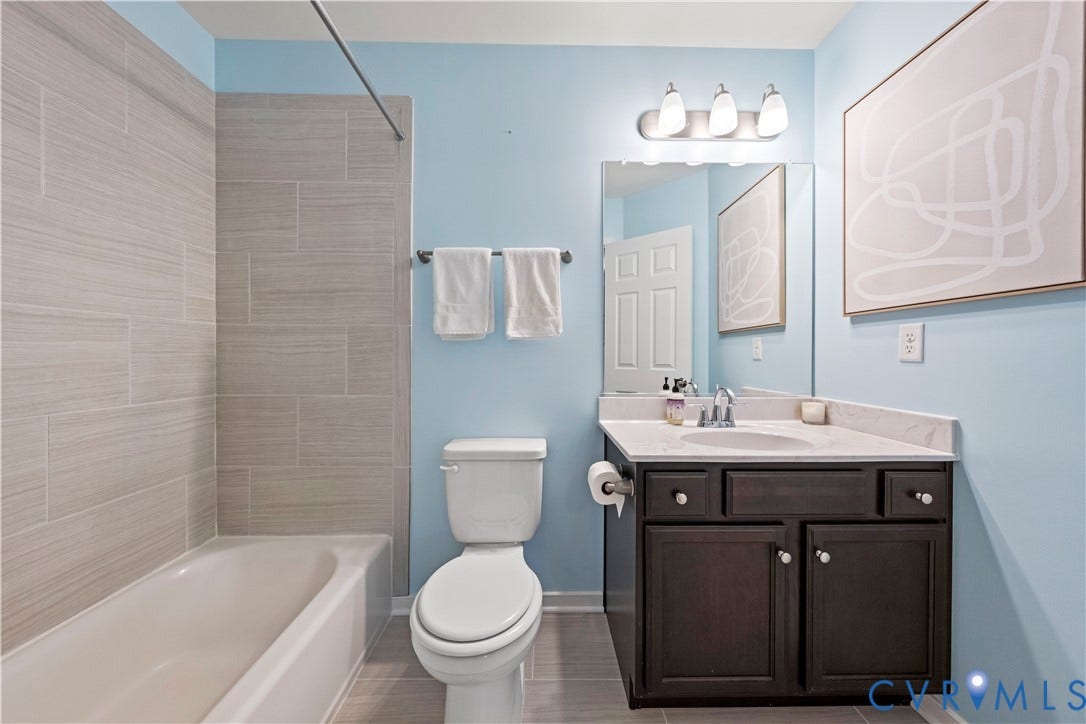 Bathroom featuring a tub/shower combination with light-toned tiled surround, a dark wood-finish vanity with a single sink, and a light countertop