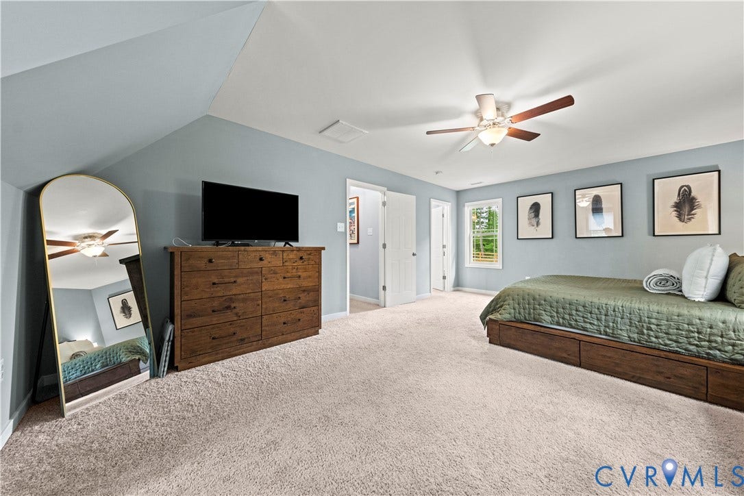 Carpeted bedroom featuring an angled ceiling, a ceiling fan with light fixture, light blue wall paint, two white doors, and a window with natural light