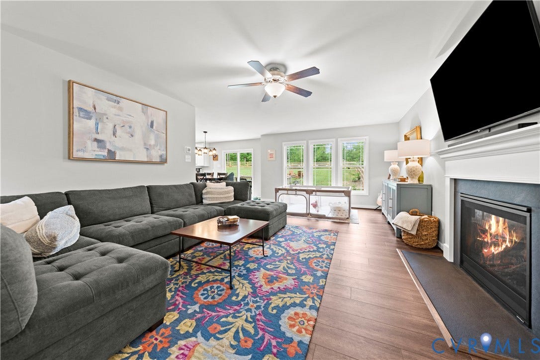Spacious living area featuring wood-finish flooring, a ceiling fan, and a fireplace with a white mantel and black hearth