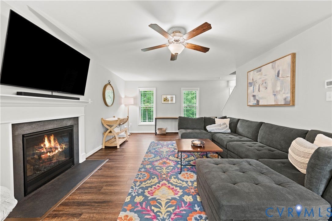Living area featuring wood-finish flooring, a white mantel fireplace with a dark stone surround, and a ceiling fan with integrated lighting