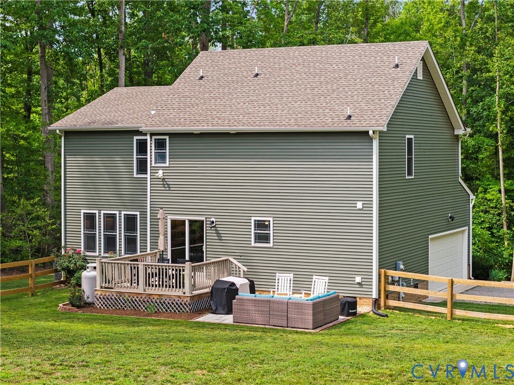 Rear exterior featuring green siding, a spacious wood deck, lower patio area, and a single-car garage with a white door