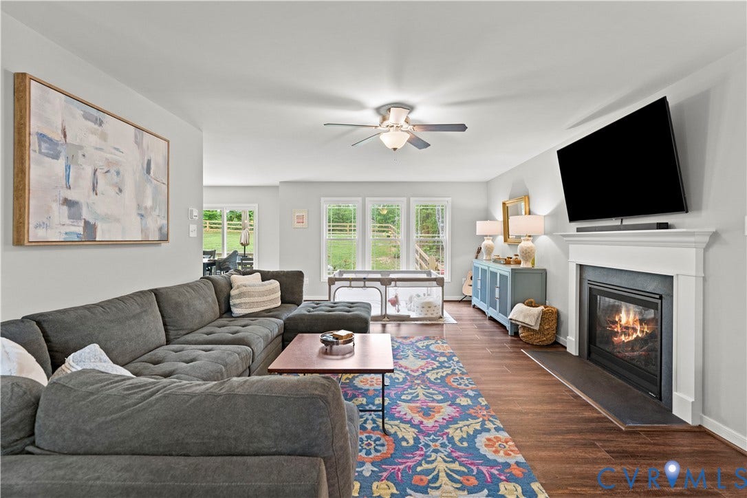 Spacious living area featuring wood-finish flooring, a white mantel fireplace, and a ceiling fan