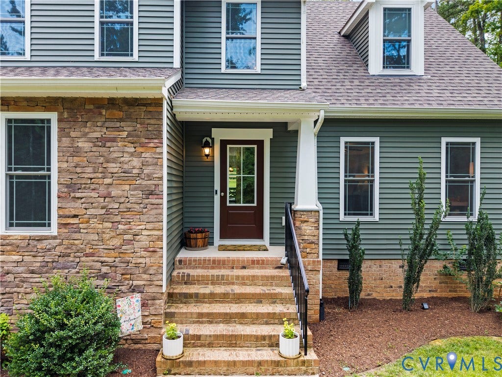 Front entry featuring a paneled door with glass inserts, brick steps, and wrought iron railing