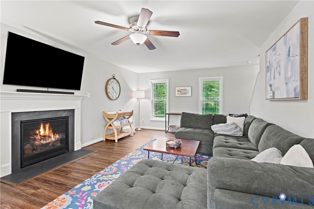 Living area featuring a fireplace with a white mantel and dark hearth, wood-finish flooring, and a ceiling fan with integrated lighting