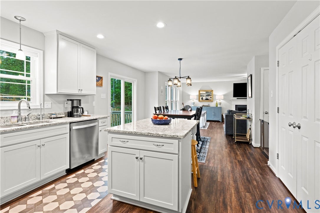 Kitchen featuring white cabinetry, light-toned granite countertops, stainless steel appliances, and a central island with bar seating