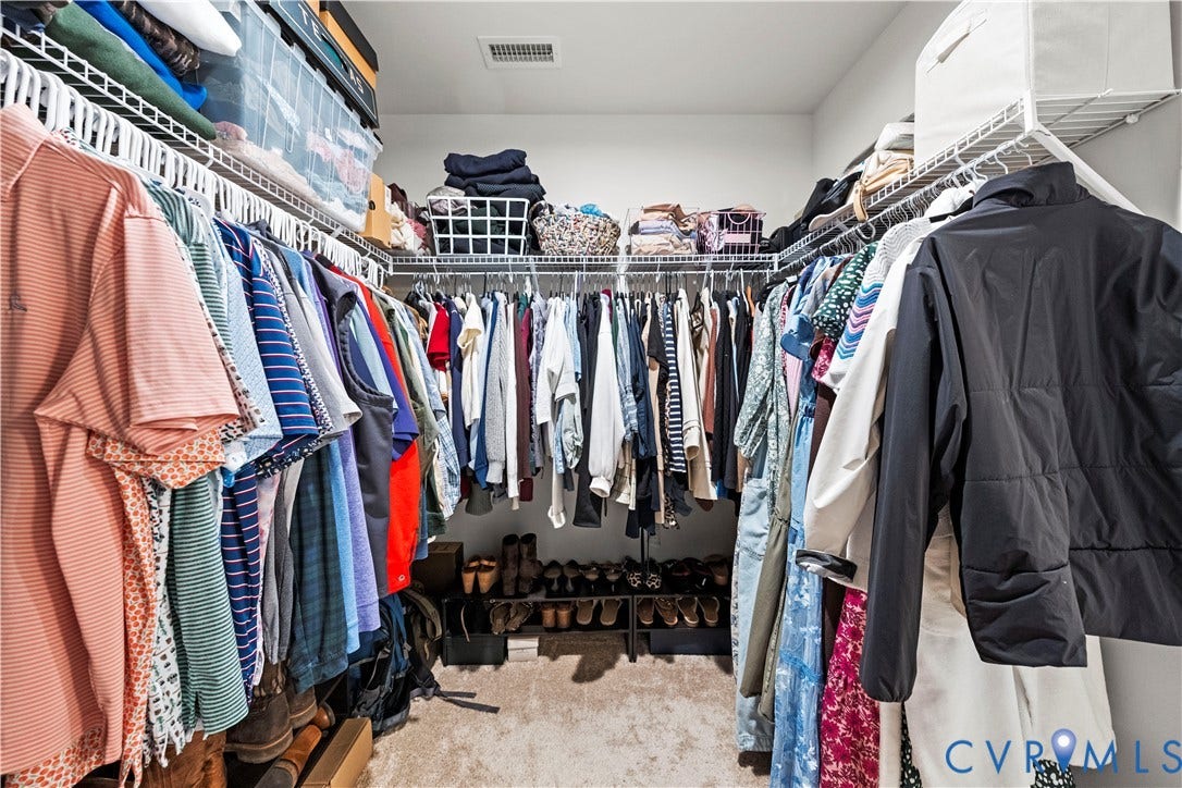 Walk-in closet featuring carpet flooring, white wire shelving, and multiple hanging rods for wardrobe organization