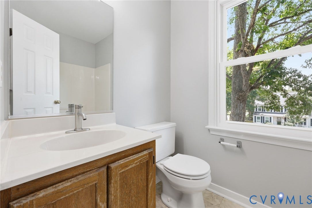 9500 Mesquite Road, Glen Allen, VA 23060 Bathroom featuring a window with a tree canopy backdrop, a light wood-finish vanity with a white countertop and integrated sink, a brushed nickel faucet, and a toilet with a dual-flush mechanism