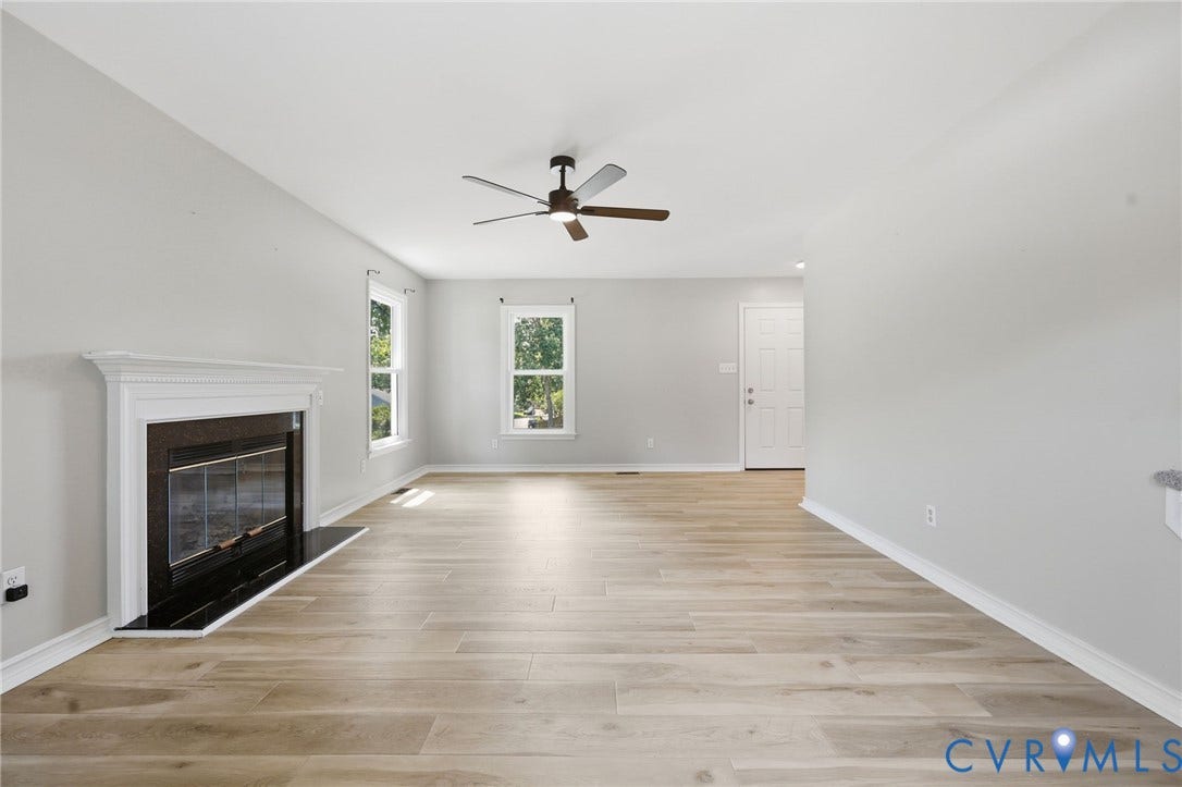 9500 Mesquite Road, Glen Allen, VA 23060 Spacious living area featuring light wood-finish flooring, a white mantel fireplace with a black surround, and a ceiling fan with integrated lighting
