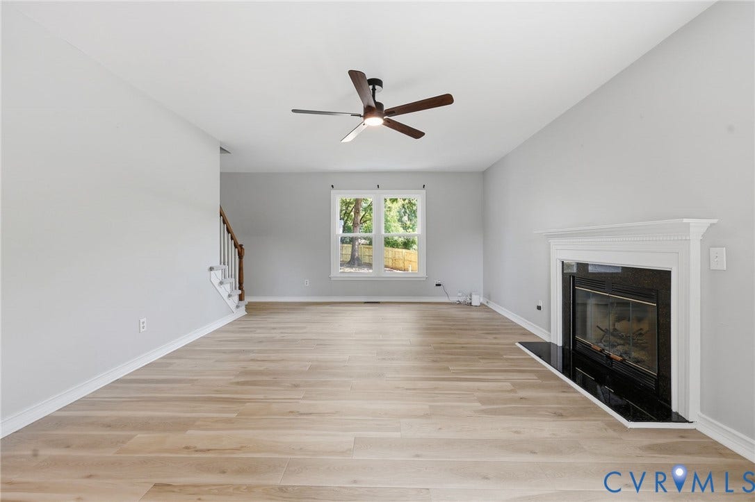 9500 Mesquite Road, Glen Allen, VA 23060 Spacious living area featuring light wood-finish flooring, a white mantel fireplace with a black hearth, a ceiling fan with integrated lighting, and neutral wall tones