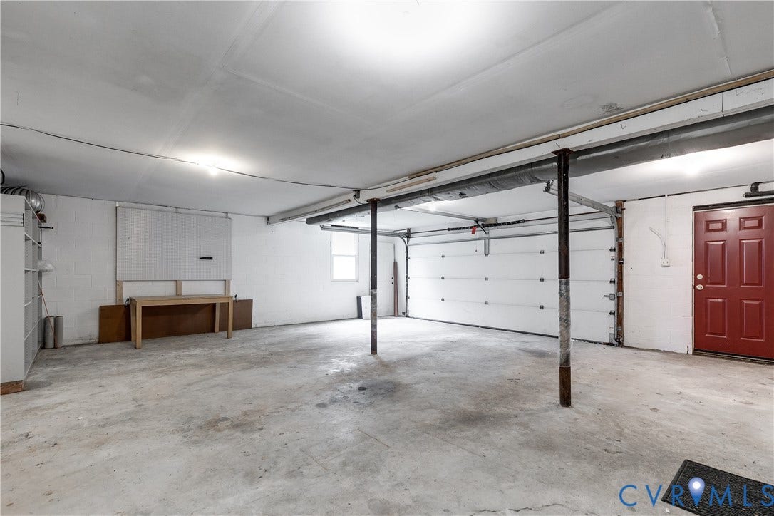 3924 Belspring Road, Chester, VA 23831 Spacious garage featuring concrete flooring, a large overhead door, a red entry door, a window for natural light, and built-in shelving